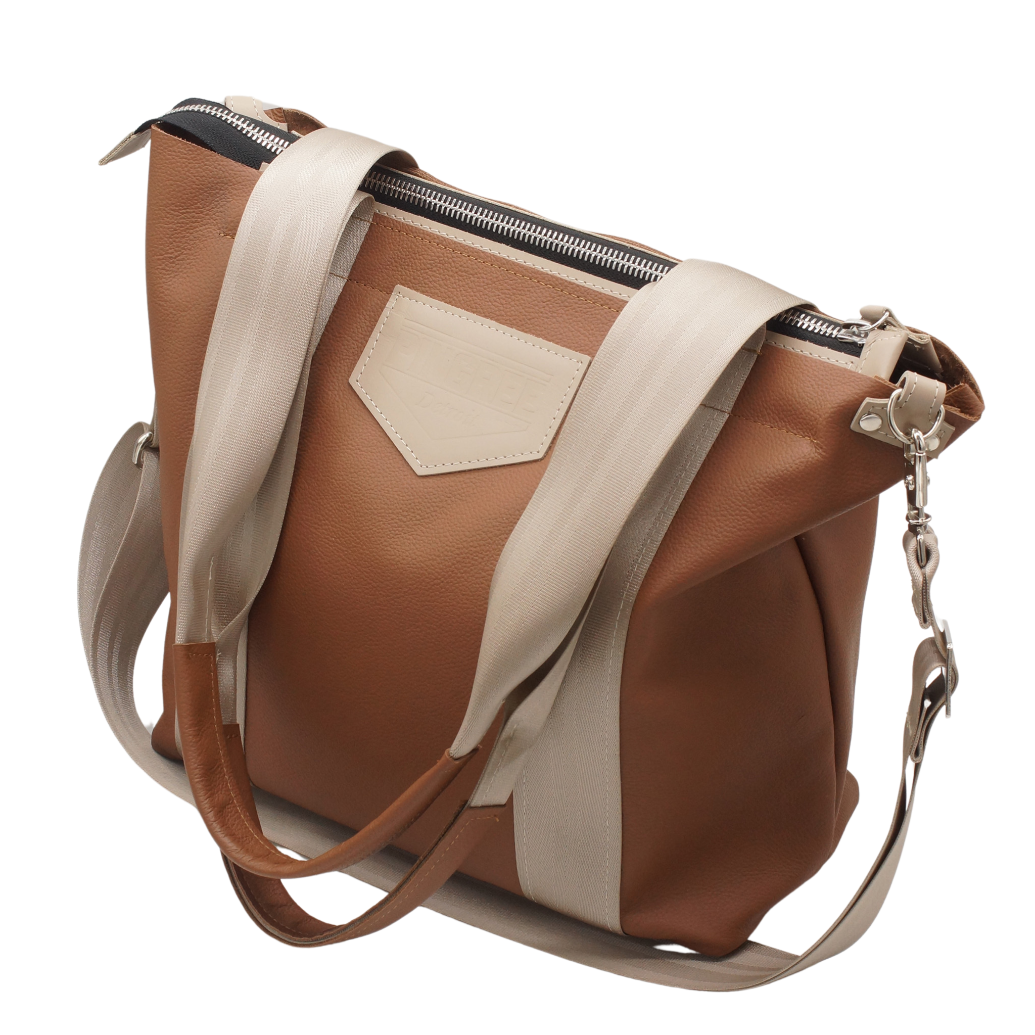 M1 Leather Work & Travel zipper Tote in hazelnut brown. Seatbelt straps accented in leather. Handmade in Detroit with leather up cycled from the Automotive industry with American Made hardware a zipper closure a detachable Crossbody strap included feet on the bottom and grateful for work or travel. Carry-on compliant.