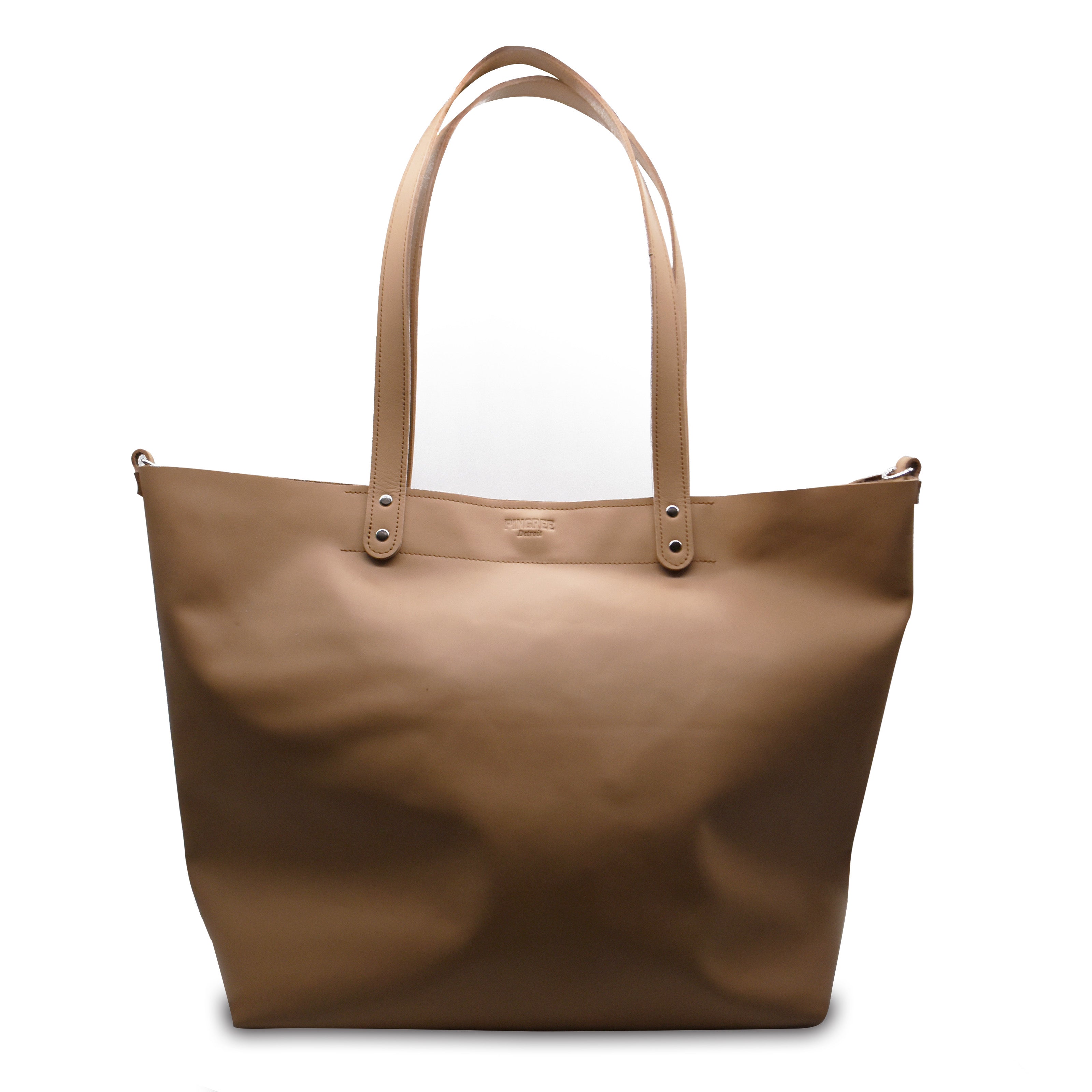 Brown tote bag with leather handles on a white background. This shopper tote bag with black accents on a white background. Made in Detroit. Leather bag crafted from upcycled automotive leather. Crossbody strap available. Bag made by Pingree Detroit. Perfect for shopping, day trips, wedding anniversaries and employee retreats and gifts.