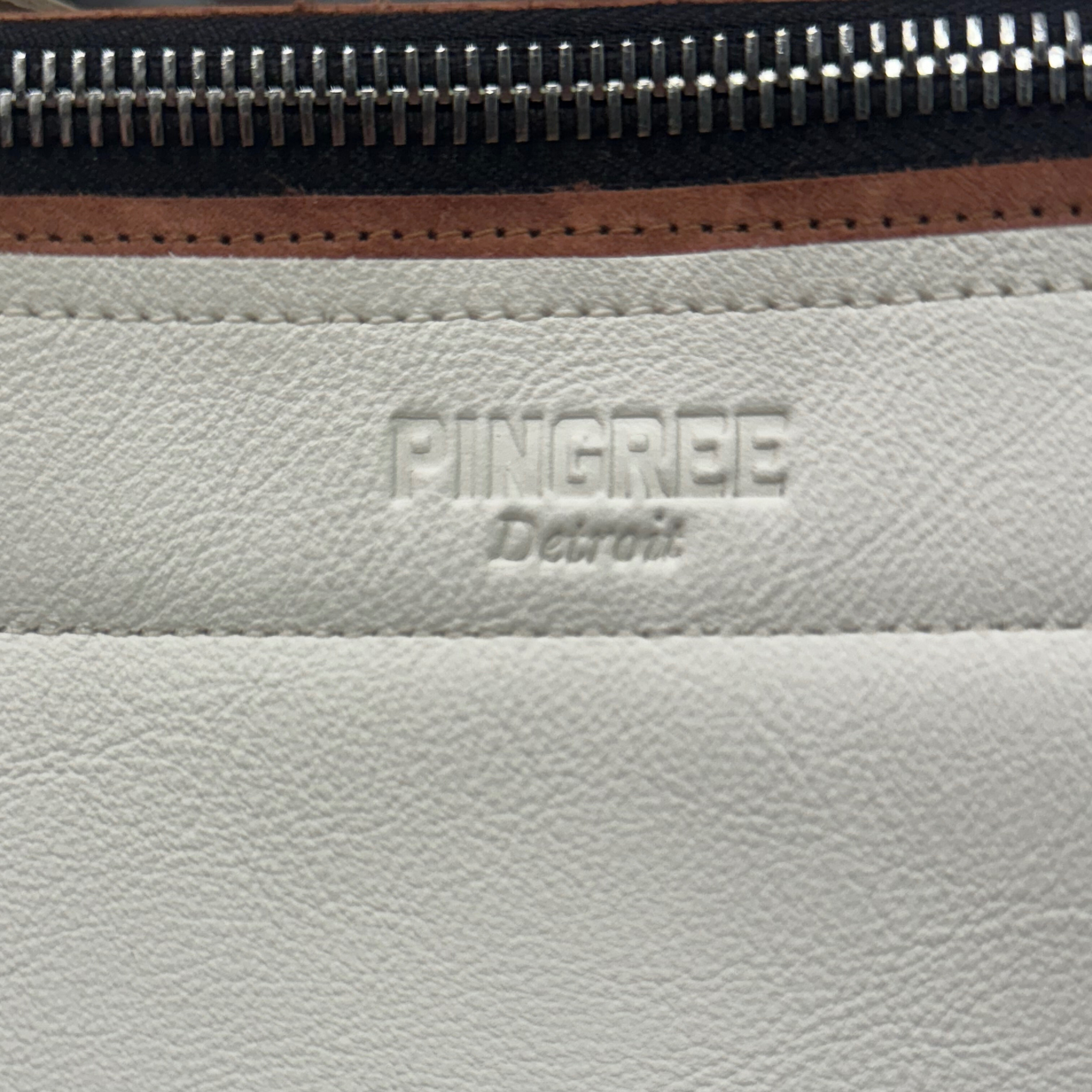 Cappuccino color leather bag and travel tote or work bag with the logo embossed and pictured here zoomed in. with a zipper and made sustainably by Pingree Detroit,
In Detroit, with upcycled leather, pictured here with the adjustable seat belt crossbody strap. Made for travel or weekender bag. Carry-on compliant.