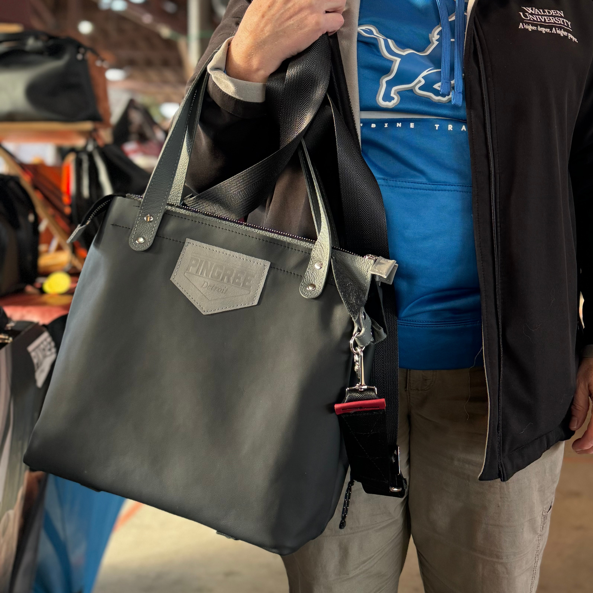 M1 Leather Work & Travel zipper Tote in black. Worn on this customers arm. Handmade in Detroit with leather up cycled from the Automotive industry with American Made hardware a zipper closure a detachable Crossbody strap included feet on the bottom and grateful for work or travel. Carry-on compliant.