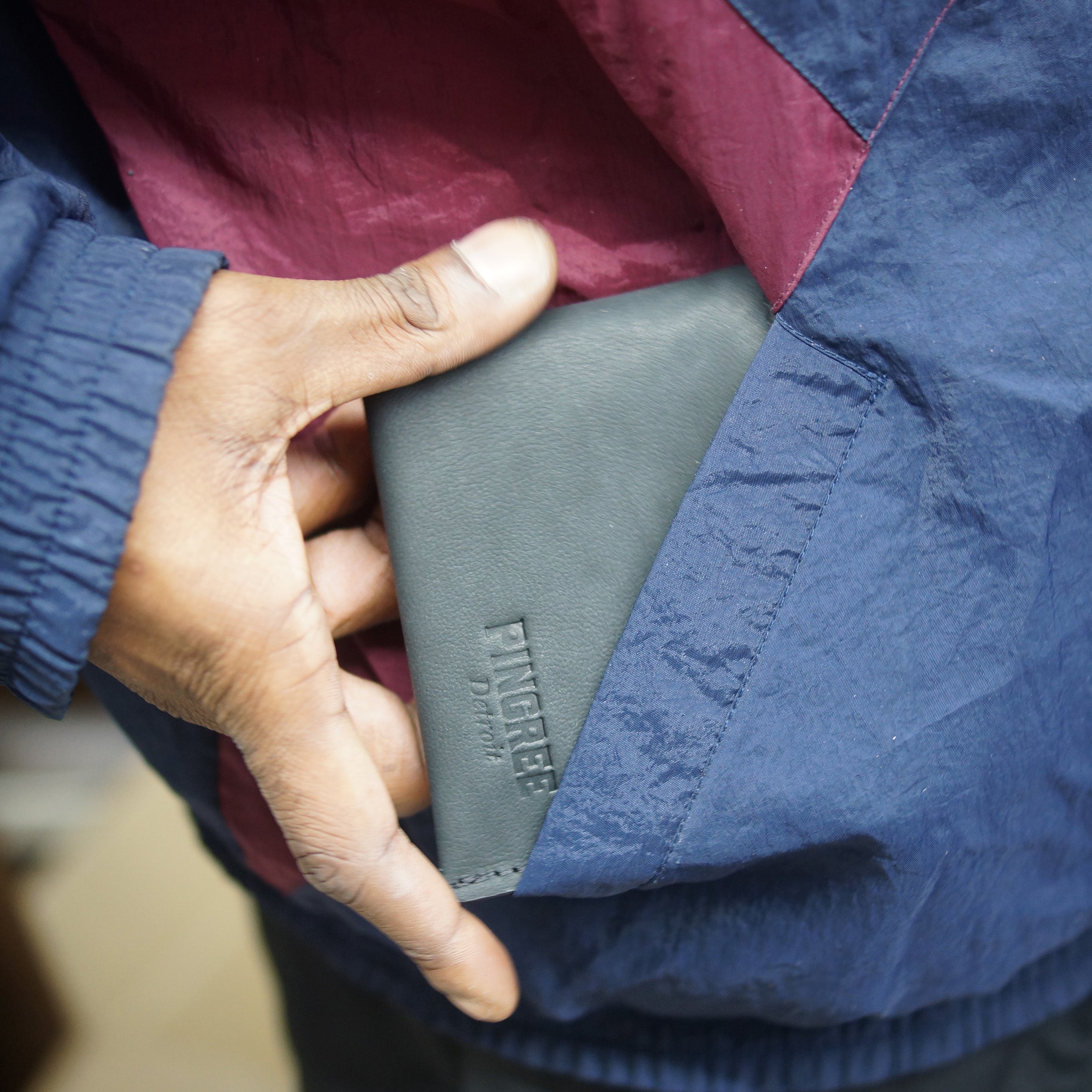 Onyx black billfold wallet, pictured here sliding into a pocket. Made in Detroit, Michigan USA. Big enough for George Costanza, 10 pockets, leather upcycled from the production of new cars, handmade in Detroit by U.S. Veterans and Detroiters. Liner made from upcycled material from the production of Army tents.