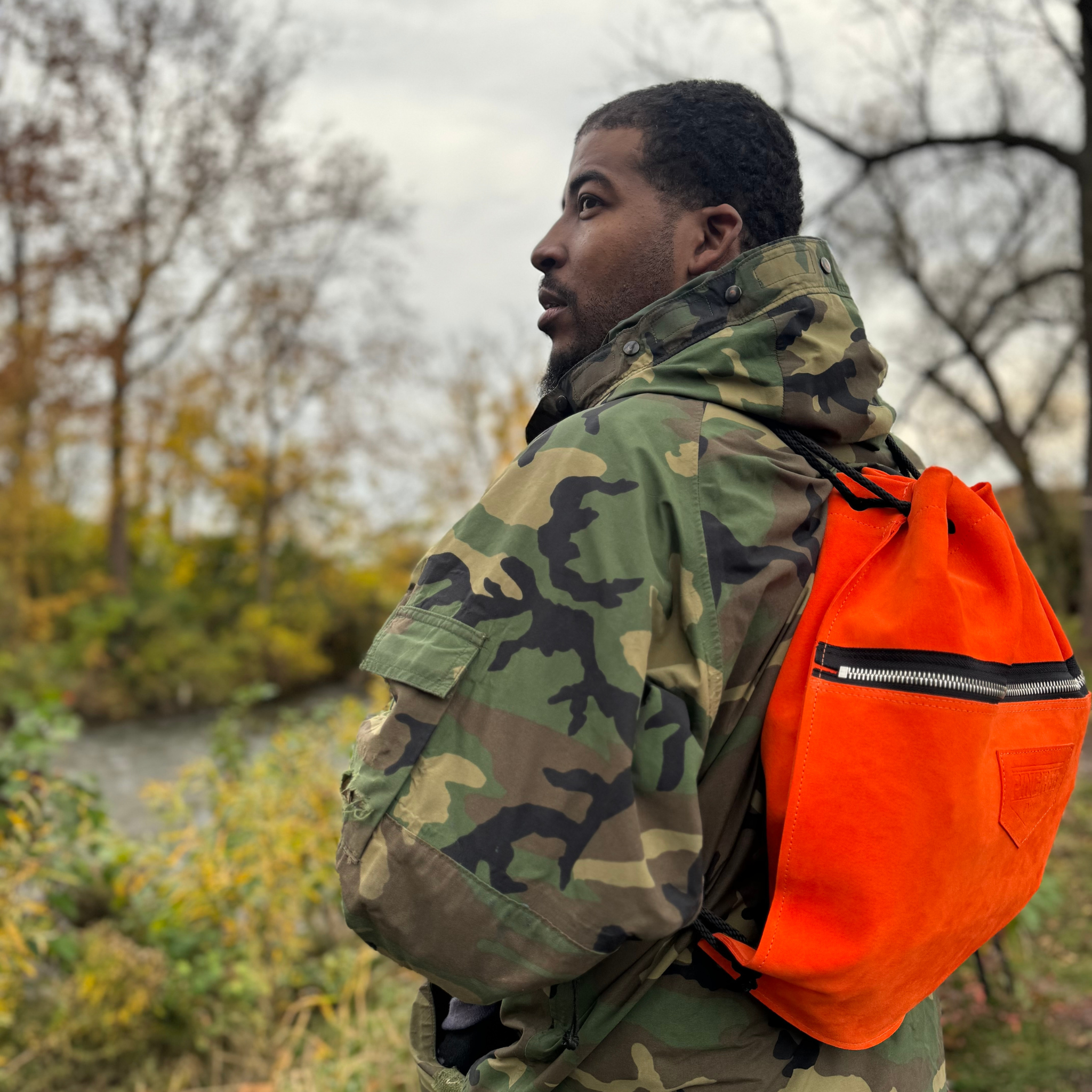 Detroit made leather drawstring bag made with upcycled leather. Pictured here n one of our Veteran co-owners of Pingree Detroit wearing his cammo jacket from the Air Force and sporting the orange Detroit Drawstring backpack.