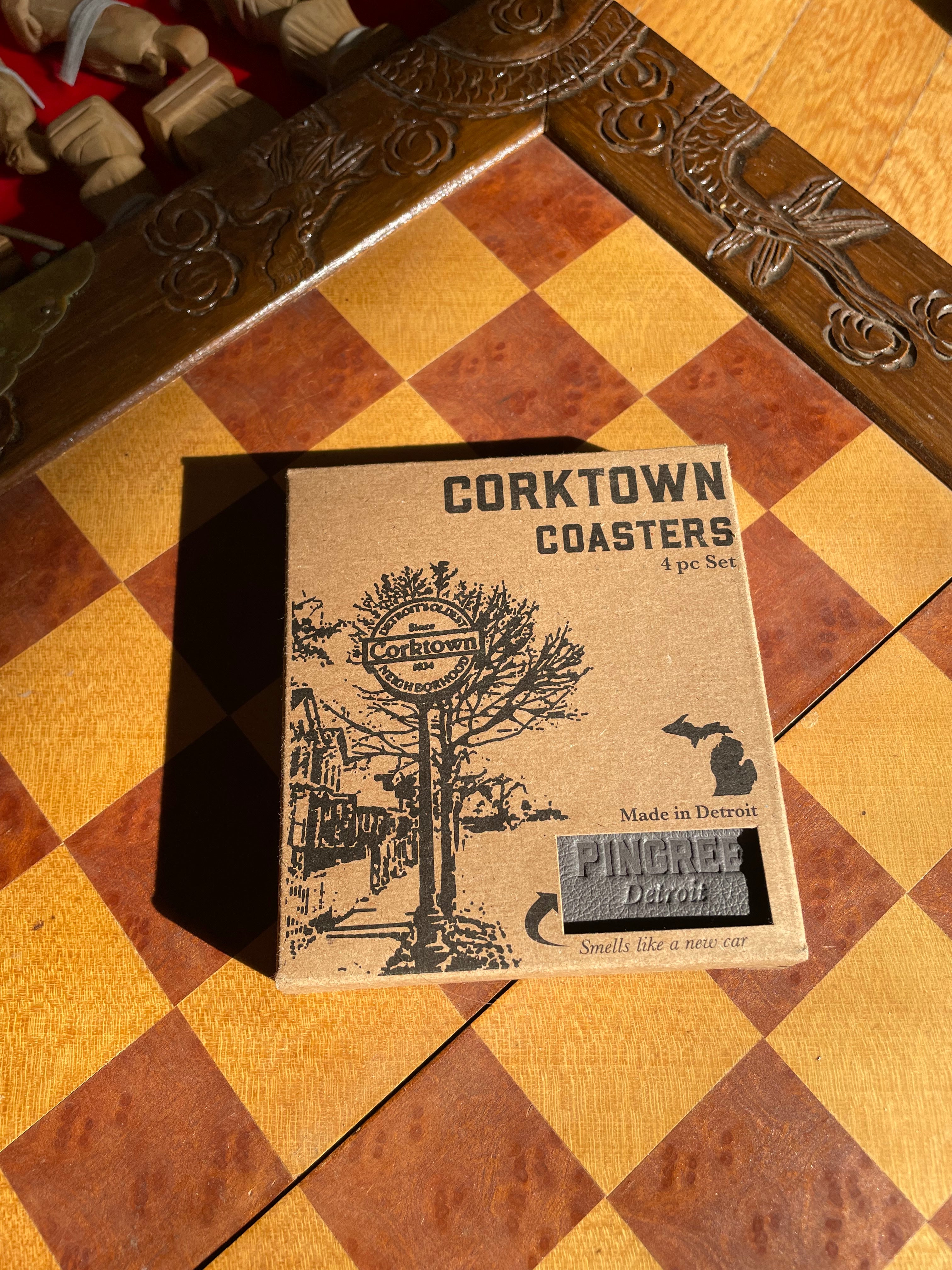 coaster box made from recycled paper with the Pingree Detroit logo visible and the cosasters made with upcycled leather and recycled cork are on a chess table ready for us.