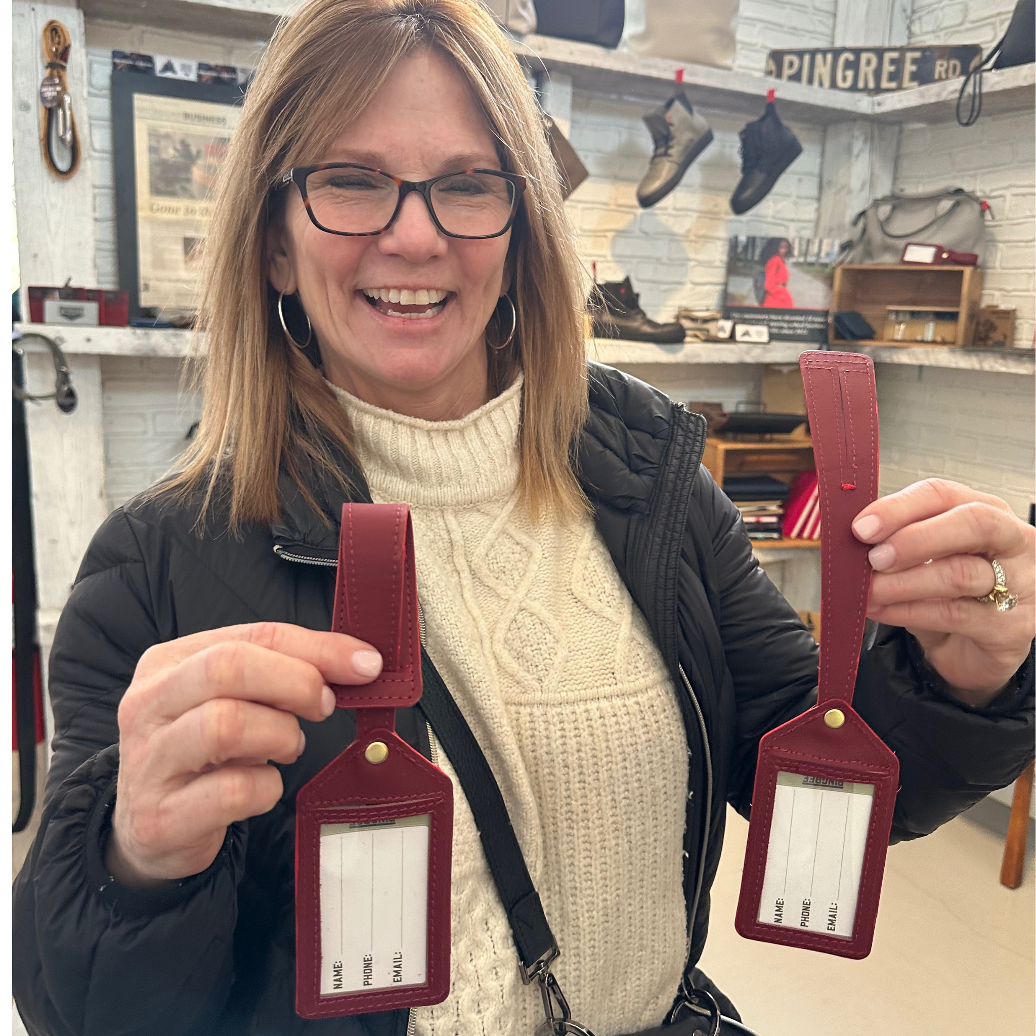 two luggage tags made by pingree detroit with car leather upcycled and a smiling person holding them at Pingree Detroit's store at the Rustbelt market in Michigan.