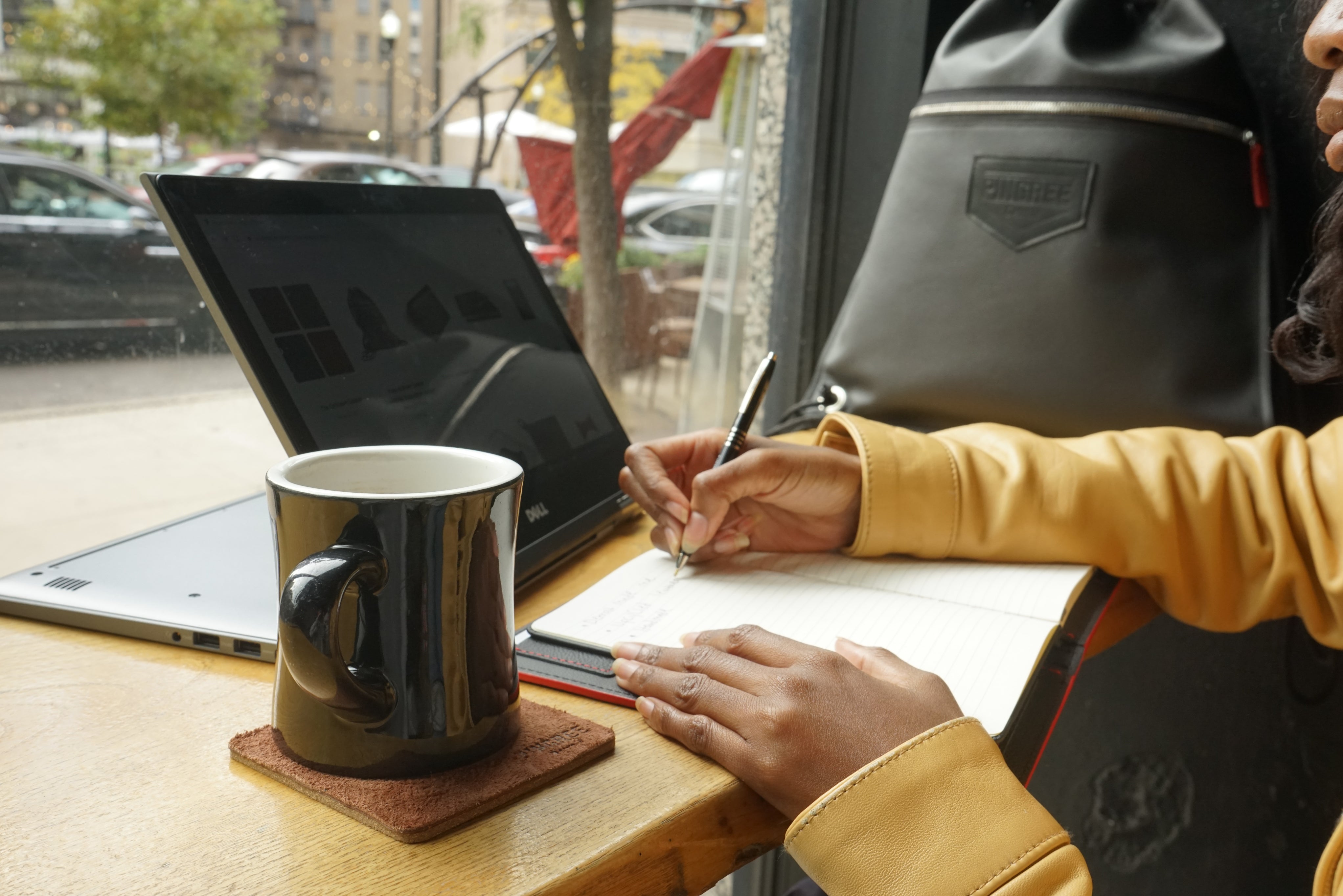 coasters, workfolio journal being used in a coffee shop, with a bag in the bckgound. All made in Detroit with upcycled car leather.