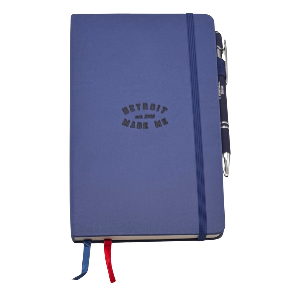 Blue notebook with 'Detroit Made Me' text and a pen on a white background. Our hand assembled Journal crafted with 100% recycled paper pulp with lined pages. Detroit made me. Includes a pen, double bookmarks a front pocket and a rear pocket and elastic closure that we sew for reinforcement. A 5 size, comparable to a moleskine style, fits inside of our portfolio or works great as a standalone.