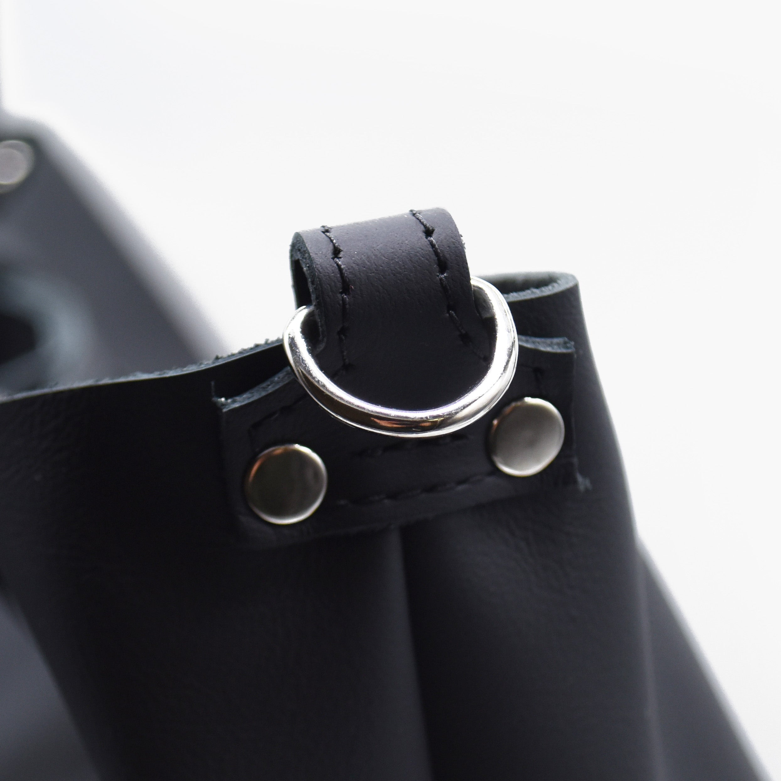 Close-up of a black leather strap with silver hardware on a white background. Black leather tote.