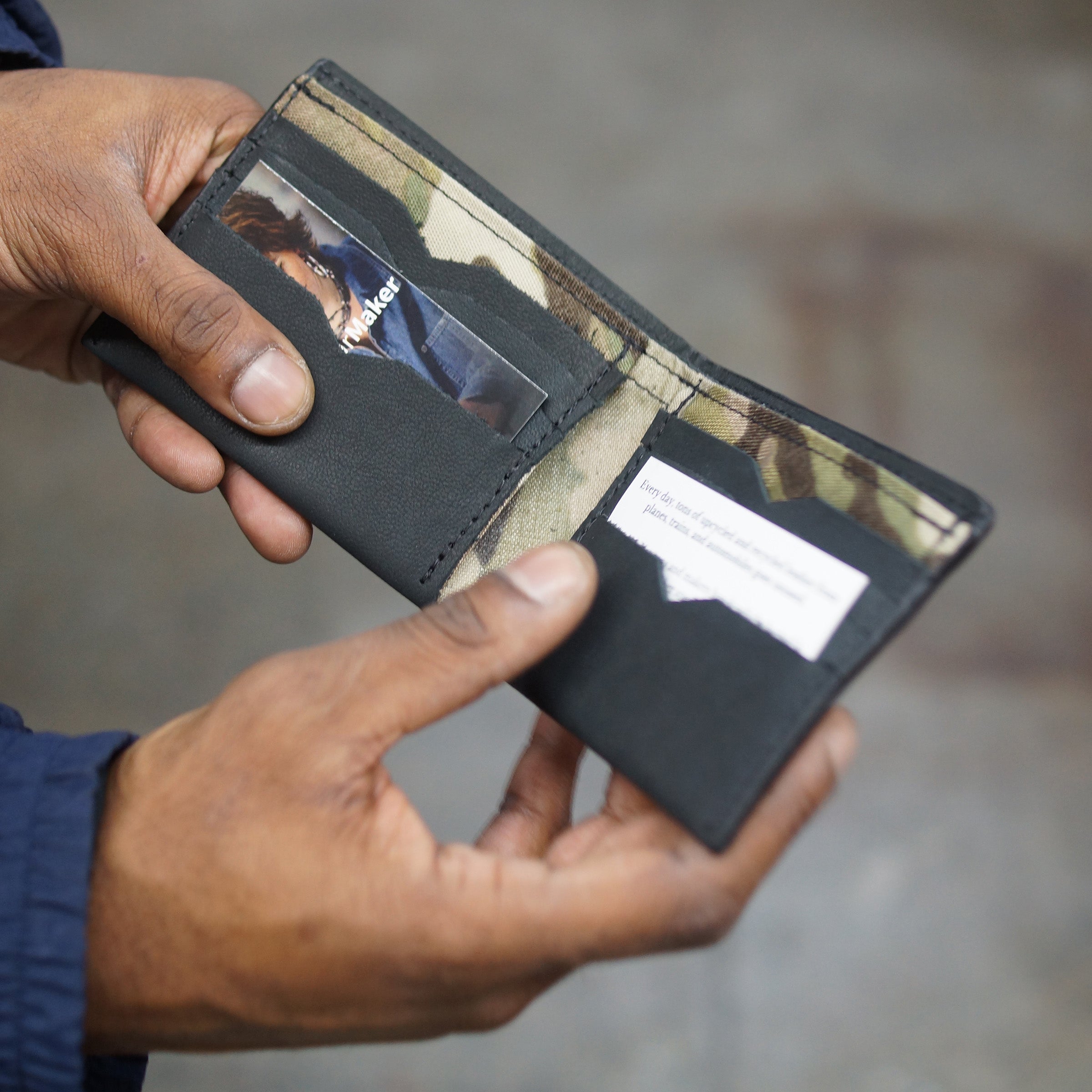 Onyx black billfold wallet, pictured here open, held in a hand. Made in Detroit, Michigan USA. Big enough for George Costanza, 10 pockets, leather upcycled from the production of new cars, handmade in Detroit by U.S. Veterans and Detroiters. Liner made from upcycled material from the production of Army tents.  