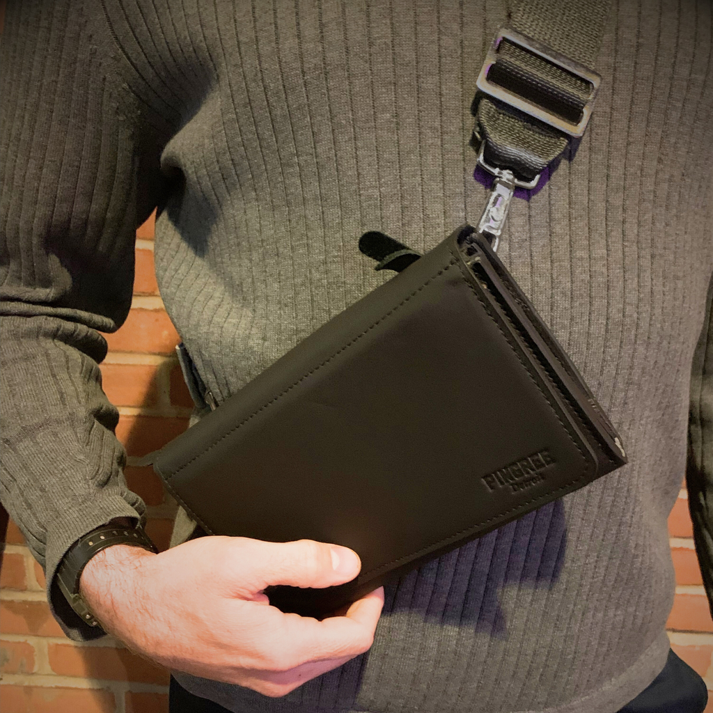 The Adeline Lux, pictured here as a crossbody on a male model, with seatbelt straps, a stone grey interior, and exterior all black leather, upcycled from the automotive industry, with clean rounded corners, magnetic closure, and a wristlet. This 5-in-1 bag is handmade in Detroit, MI USA, with upcycled leather from the automotive industry. Each comes with a picture of the Veteran or Detroiter who made it. 