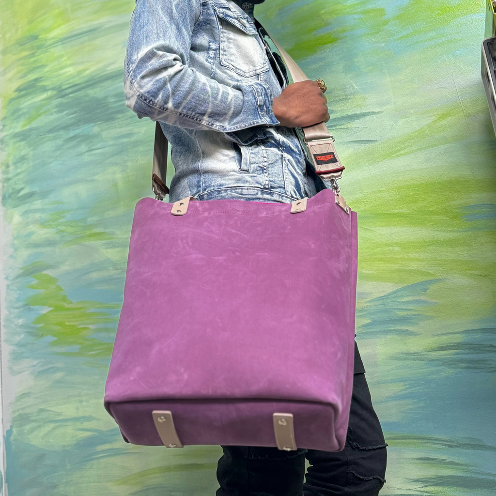 Purple leather bag and travel tote or work bag with a zipper and made sustainably by Pingree Detroit,
In Detroit, with upcycled leather, pictured here with the seat belt crossbody strap. Shows leather bottom protective feet. Guaranteed for life.