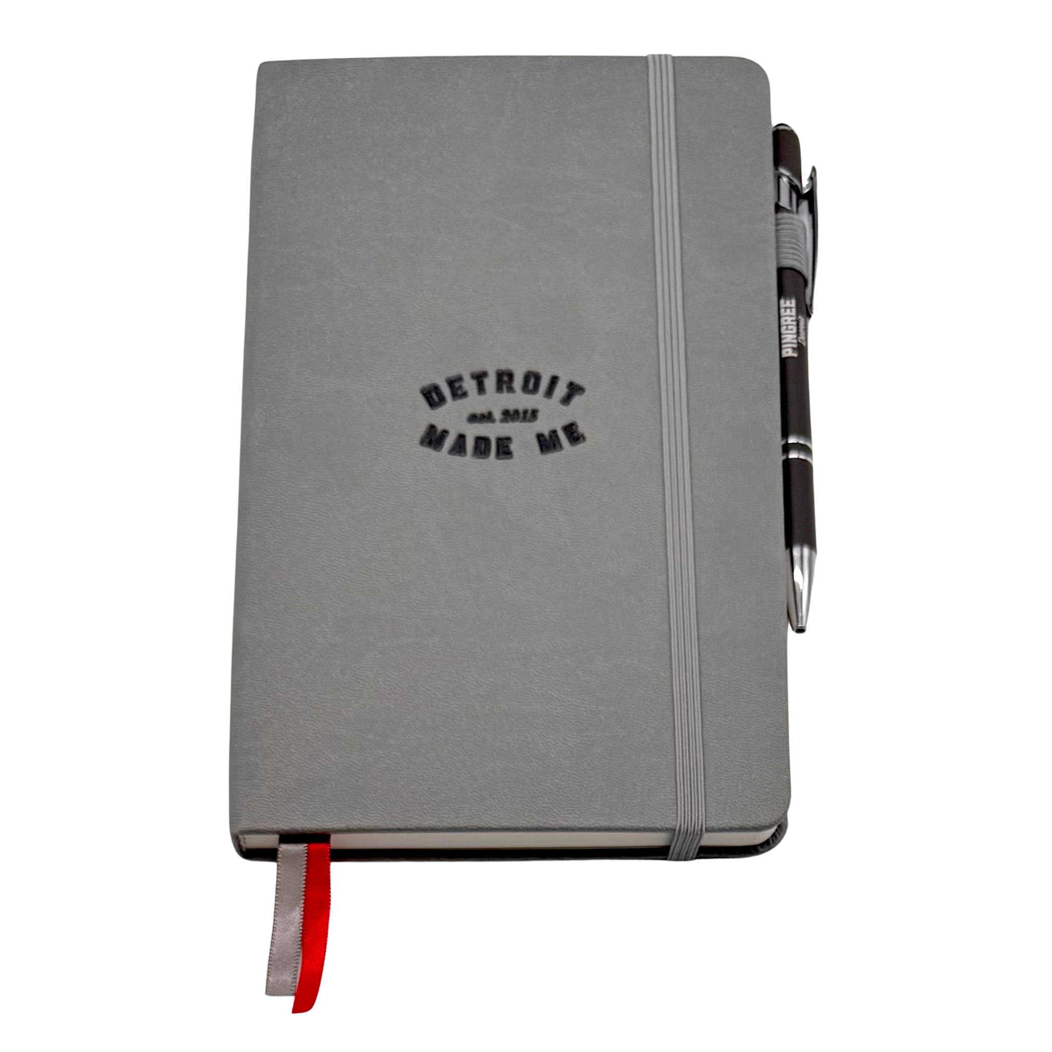 Gray notebook with 'Detroit Made Me' text and a pen on a white background. Our hand assembled Journal crafted with 100% recycled paper pulp with lined pages. Detroit made me. Includes a pen, double bookmarks a front pocket and a rear pocket and elastic closure that we sew for reinforcement. A 5 size, comparable to a moleskine style, fits inside of our portfolio or works great as a standalone.