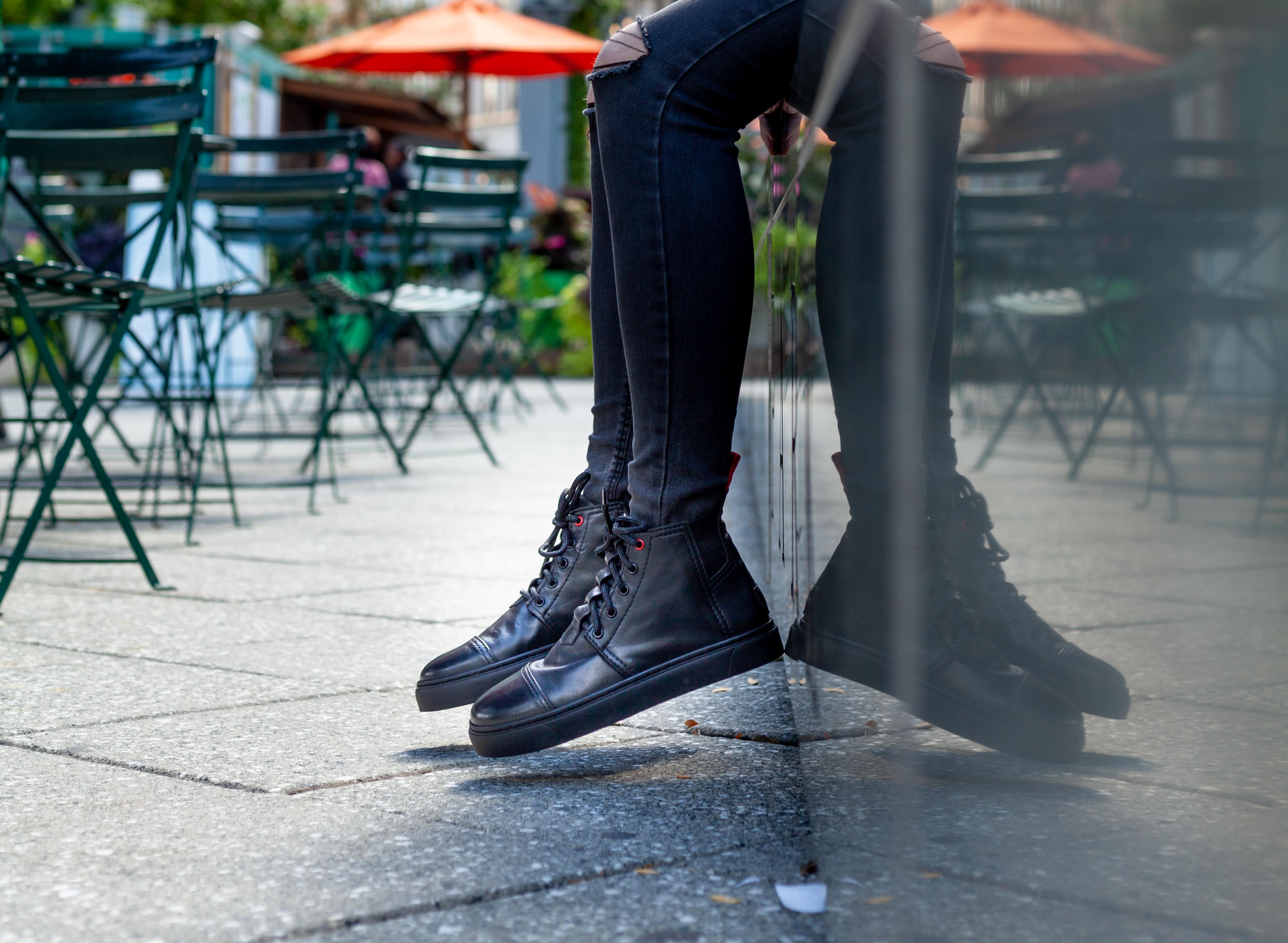 Handmade sneakers with a reflection against a wall. Black urban utility high top sneakers made in detroit with leather upcycled from new cars.