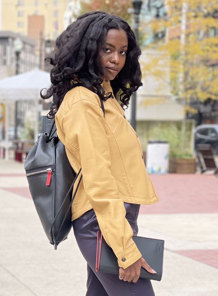 Woman holding a workfolio leather journal padfolioand wearing our leather drawstring bag, and sneakers, handmade by US Veterans and Detroiters all black leather. Both journals come with a pen made by Skilcraft. 
