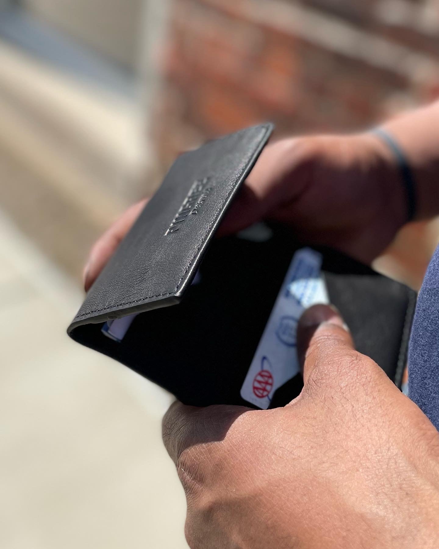 holding a leather wallet with three card slots- each holding 4-6 cards and a place for cash. Upcycled leather from new cars and handmade by US Veterans and Detroiters.