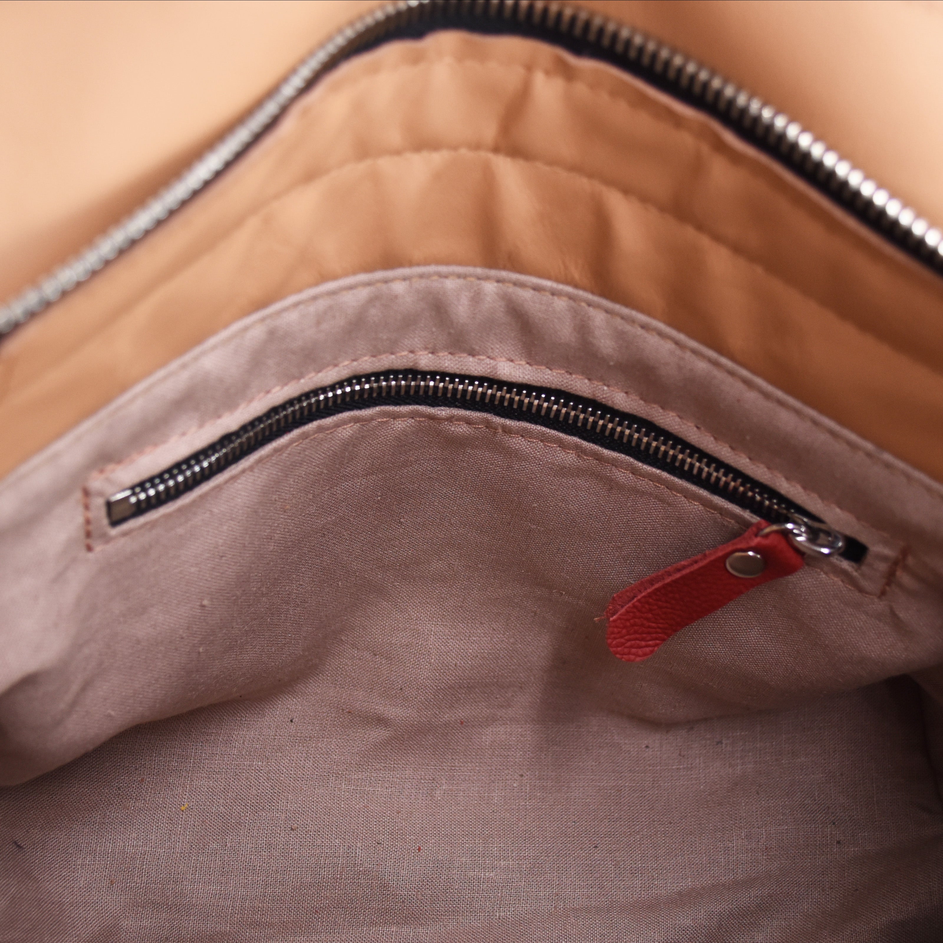 Close-up of a brown leather bag with a red zipper pull.
