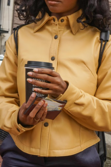 Woman holding a coffee and a Whittier Wallet. Whittier Wallet is made in the USA from repurposed materials.