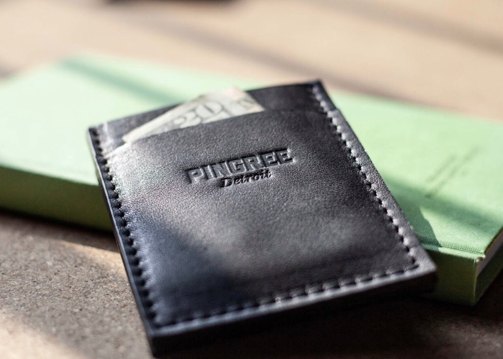 Pingree slim wallet with money on a table with a book. Made in the USA with leather sustainably sourced form automotive waste.