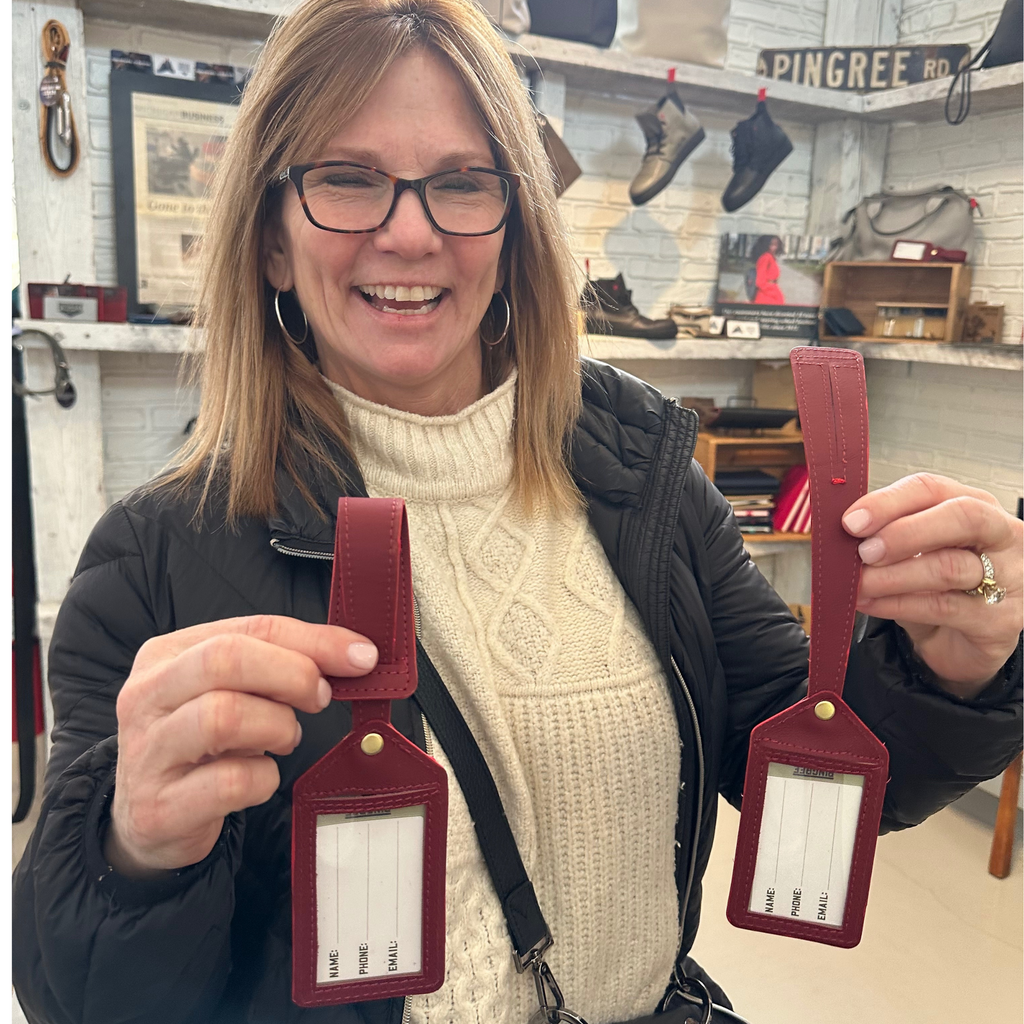two luggage tags made by pingree detroit with car leather upcycled and a smiling person holding them at Pingree Detroit's store at the Rustbelt market in Michigan. 